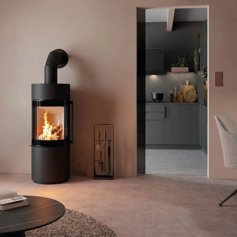 Spartherm Passo XS kompakt sort sylindrisk vedfyrt peisovn med buet glassfront og oransje flammer i moderne stue hos Peisbutikken.no
